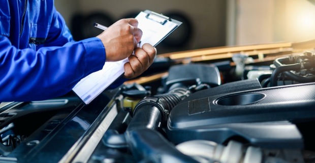 Der Mechaniker schreibt auf eine Zwischenablage, während er den Automotor betrachtet, um die Reparatur und Wartung des Autos zu bewerten.