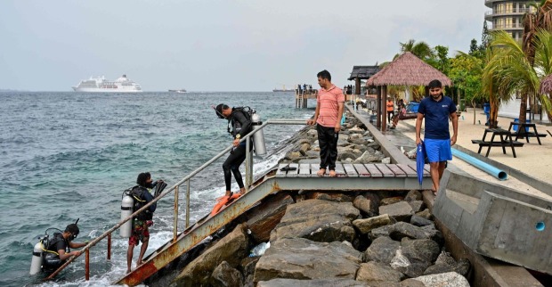 Taucher und Einsatzkräfte nach Tauchunfall auf den Malediven steigen an Küste aus dem Wasser, Rettungseinsatz im Hintergrund