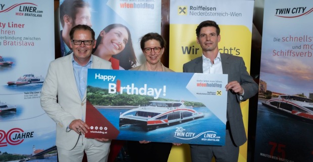 Drei Personen halten ein Jubiläumsschild zu "20 Jahre Twin City Liner"