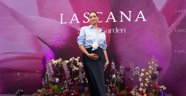 Amira Aly präsentiert ihren Babybauch bei einem Event und posiert lächelnd vor einer Blumenwand. Die schwangere Moderatorin erwartet ihr erstes gemeinsames Kind mit Christian Düren.