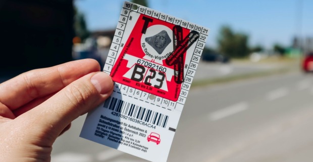 Hand hält gültige 10-Tages-Vignette für Österreich vor einer Straße als Symbol für Mautpflicht und Autobahngebühr