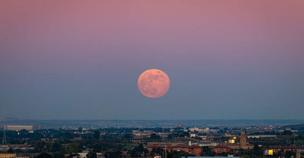 Erdbeermond 2026 als rötlicher Vollmond tief über dem Horizont bei Sonnenuntergang