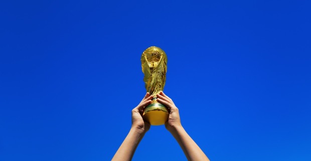 Ein Blatt hebt die Weltmeisterschafts-Trophäe oben an, einzeln gegen einen blauen Sommerhimmel.