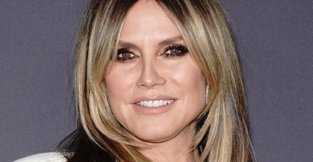 Heidi Klum lächelt bei einem öffentlichen Auftritt in die Kamera. Das Topmodel trägt ein weißes Outfit und ihre blonden Haare mit dunklem Ansatz offen.