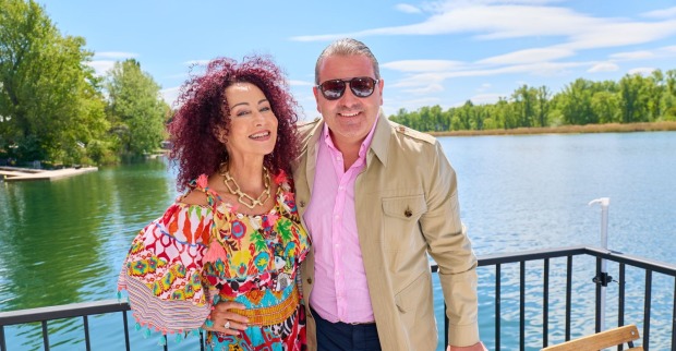 Christina Mausi Lugner und Schwiegersohn Leo Lugner lächeln gemeinsam auf einer Terrasse am Wasser im Wiener Strandcafé