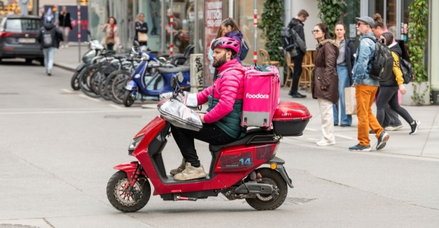 Ein Essenslieferant fährt mit einem E-Moped durch die Wiener Innenstadt