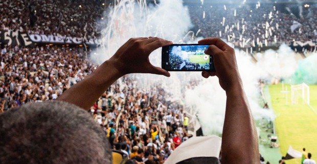 Fußballfan filmt mit seinem Smartphone die Stimmung und Pyrotechnik auf der Tribüne eines Fußballstadions./Dynamo Dresden verschärft die Regeln für Influencer und Vlogger im Stadion. Kommerzielle Aufnahmen benötigen eine Genehmigung.