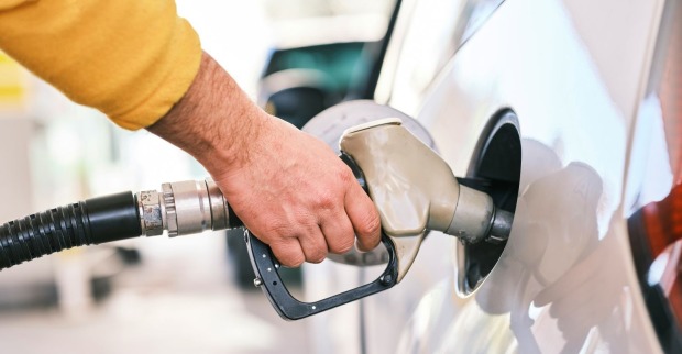 Hand eines Autofahrers mit gelbem Pullover beim Tanken eines weißen Autos
