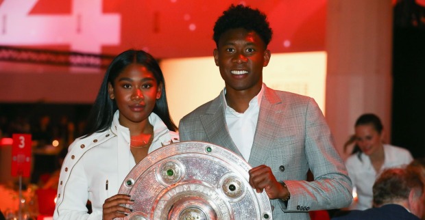 David Alaba posiert gemeinsam mit seiner Schwester Rose May Alaba und der Meisterschale des FC Bayern München bei einer Veranstaltung.