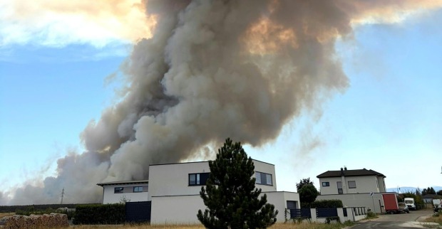 Waldbrand in St. Egyden: Dichte Rauchsäule steigt hinter Wohnhäusern einer Siedlung auf.