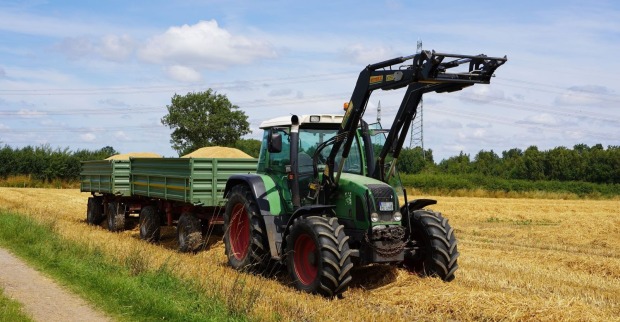 Grüner Traktor mit Anhänger auf einem Feld als Symbolbild für einen tödlichen Arbeitsunfall mit Traktor bei Mulcharbeiten im Bezirk Liezen.