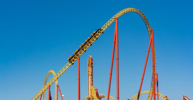 Symbolbild einer Achterbahn in einem Freizeitpark vor blauem Himmel