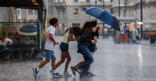 Menschen laufen bei Starkregen mit einem Regenschirm durch eine italienische Stadt.