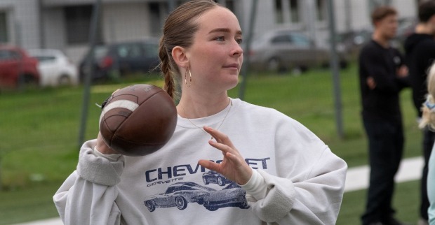 Mädchen in grauem Pullover hält einen American Football zum Wurf bereit