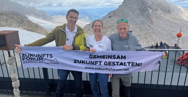 Drei Personen halten eine Banner vor einem Bergpanorama