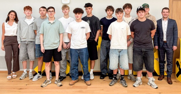 Eine Gruppe junger Workshop-Teilnehmender und zwei Erwachsene steht gemeinsam für ein Gruppenfoto in einem Innenraum.
