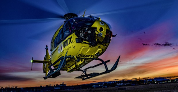 Gelber ÖAMTC-Notarzthubschrauber fliegt vor grauem Himmel.