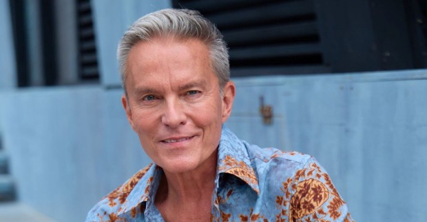ORF-Star Alfons Haider lächelt in einem blau-orange gemusterten Hemd in die Kamera. Der Entertainer sorgt mit einem Photoshop-Foto im rosa Dirndl für Aufsehen.