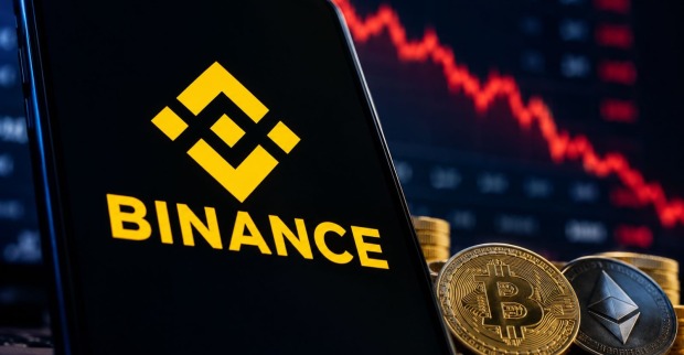 Binance-Logo auf einem Smartphone neben Bitcoin- und Ethereum-Münzen vor fallendem Kurschart als Symbolbild für den Binance Hackerangriff.