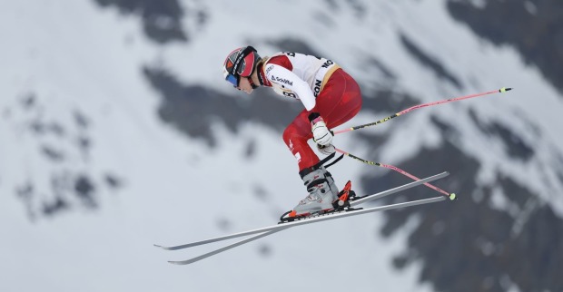 Christina Födermayr im rot-weißen Rennanzug bei einem Sprung im Skicross vor verschneiter Bergkulisse.