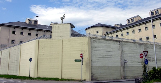 Außenansicht der Justizanstalt Graz-Karlau in Graz mit hohen Gefängnismauern, Stacheldraht und Gebäuden im Hintergrund.