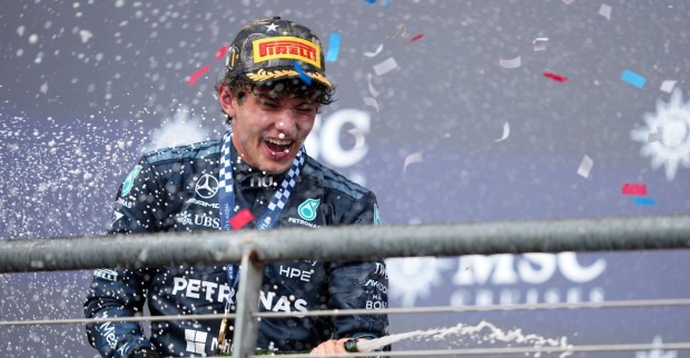 Mercedes-Pilot Kimi Antonelli jubelt auf dem Siegerpodest mit Pirelli-Kappe und Medaille, während Champagner spritzt und Konfetti fällt.