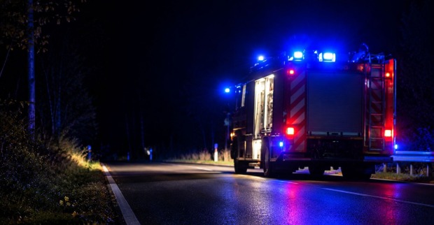 Feuerwehrfahrzeug mit eingeschaltetem Blaulicht auf einer dunklen Landstraße bei Nacht.