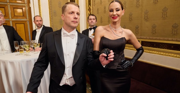 Sandy Meyer-Wölden in einem schwarzen, schulterfreien Abendkleid mit langen Handschuhen bei einer eleganten Veranstaltung neben Oliver Pocher im Frack.