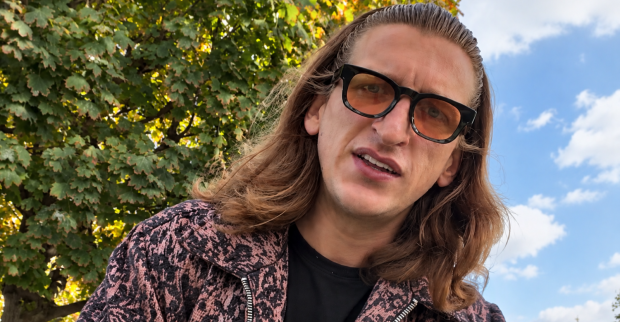 Satans Bratan mit langen Haaren, getönter Sonnenbrille und gemusterter Jacke im Freien. Der österreichische Influencer wehrt sich auf Instagram gegen Hater.