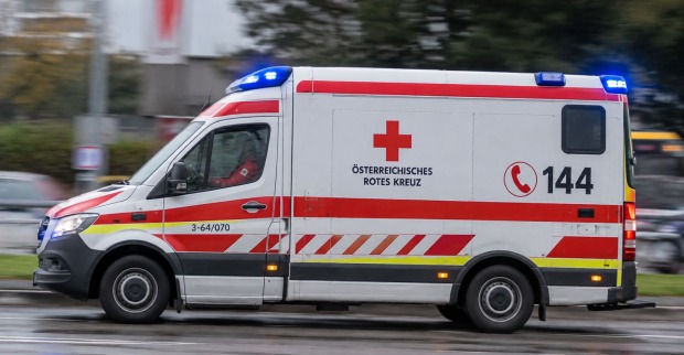 Rettungswagen des Österreichischen Roten Kreuzes mit eingeschaltetem Blaulicht, seitlich auf einer Straße aufgenommen, KI-Themenbild.