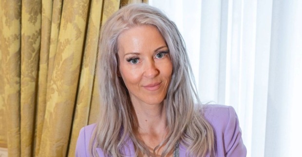 Simone Lugner, Witwe von Richard Lugner, mit langen blonden Haaren und lilafarbenem Blazer auf einem Porträtfoto.