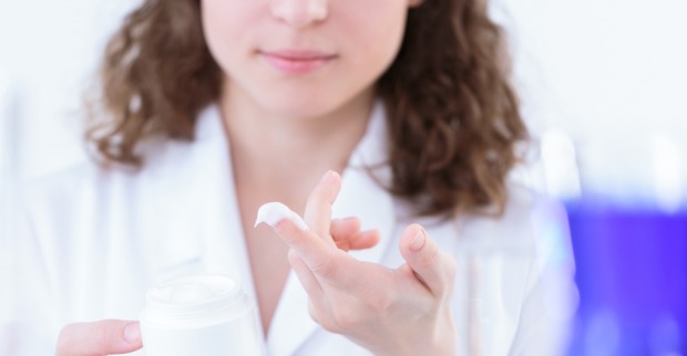 Eine junge Frau im weißen Kittel hat mit dem Finger Creme aus einem Tiegel entnommen