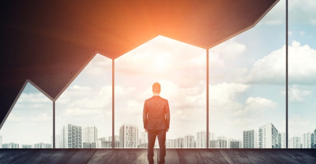 Ein Mann steht vor einem wie ein steil nach oben verlaufender Aktienkurs gestalteten Panoramafenster, durch das er die aufgehende Sonne beobachtet