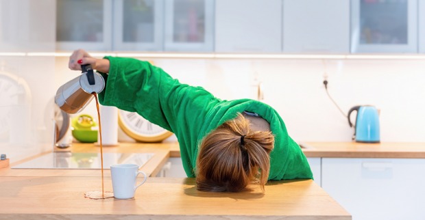 Müde Frau hat ihren Kopf auf die Tischplatte gelegt und verschüttet beim Einschenken den Kaffee | Credit: iStock.com/morgan23