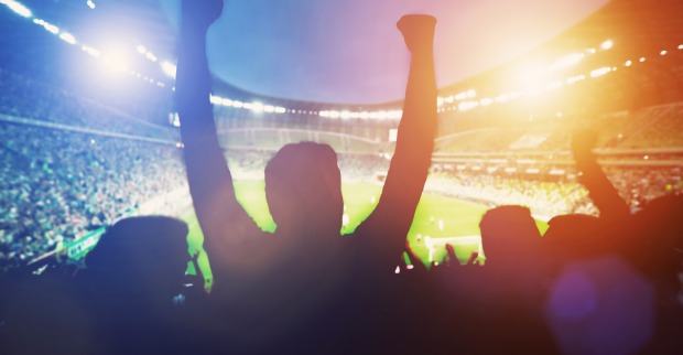 Die Silhouetten mehrerer Fußballfans in einem hell erleuchteten Stadion