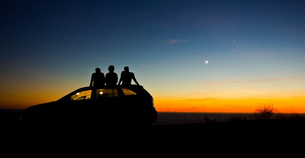 Drei junge Menschen sitzen auf dem Dach ihres Autos und genießen den Sonnenuntergang | Credit: iStock.com/antolikjan