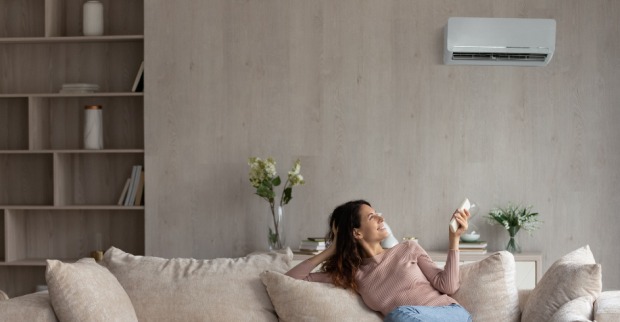 Junge Frau reguliert per Fernbedienung die Klimaanlage in ihrer Wohnung | Credit: iStock.com/fizkes