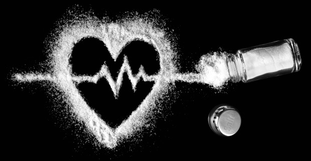 Ein umgekippter Salzstreuer mit dessen Inhalt ein Herz samt EKG Linie auf einen schwarzen Hintergrund gemalt wurde
