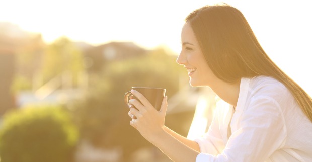 Glückliche Hausbesitzerin mit einer Tasse Kaffee auf ihrem Balkon | Credit: iStock.com/AntonioGuillem