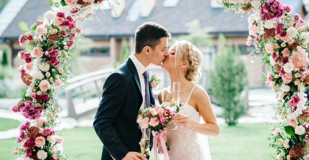 Ein Brautpaar beim Hochzeitskuss unter einem Blumenbogen