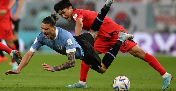 Ein südkoreanischer Fußballspieler bringt einen Gegner aus Uruguay zu Fall