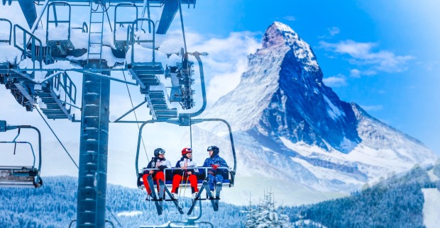 Drei Menschen fahren in Zermatt mit dem Sessellift. | Credit: iStock.com/Sinenkiy