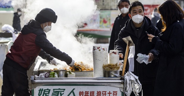 Aufnahme einer chinesischen Straßenküche, in der ein Verkäufer mehreren Passanten Essen reicht