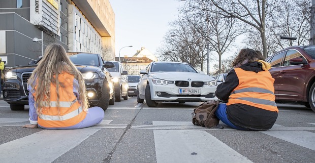 Klimaaktivisten sitzen in einer orangen Warnweste auf der Straße