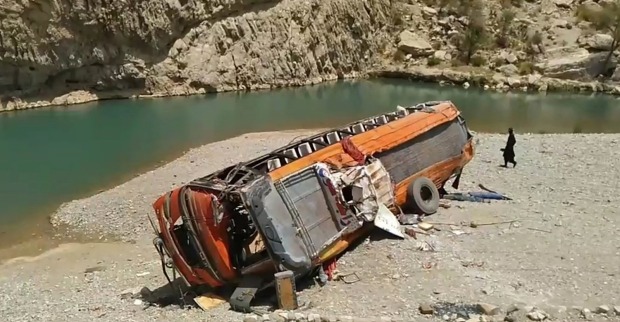 Ein in eine Schlucht gestürzter orangefarbener Bus, der auf einer Sandbank vor einem Fluss zu liegen gekommem ist