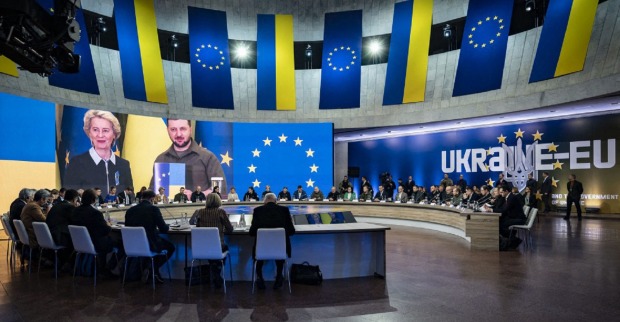 Gipfeltreffen: Sitzungssaal, gerahmt von ukrainischen und europäischen Flaggen. Von der Leyen und Selenskyi sind auf einem darüberhängendem Bildschirm eingeblendet.