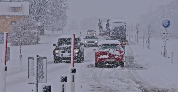 Eine tiefverschneite Straße. Autos bewegen sich auf der Schneefahrban, seitlich das Verkehrsschild für Schneeketten
